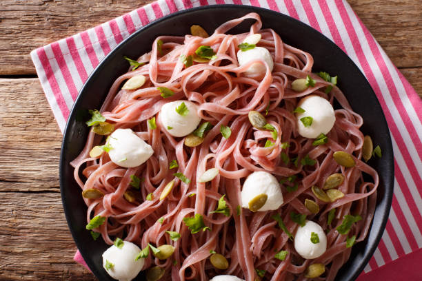 Beetroot pasta with mozzarella cheese, pumpkin seeds and parsley closeup. horizontal top view