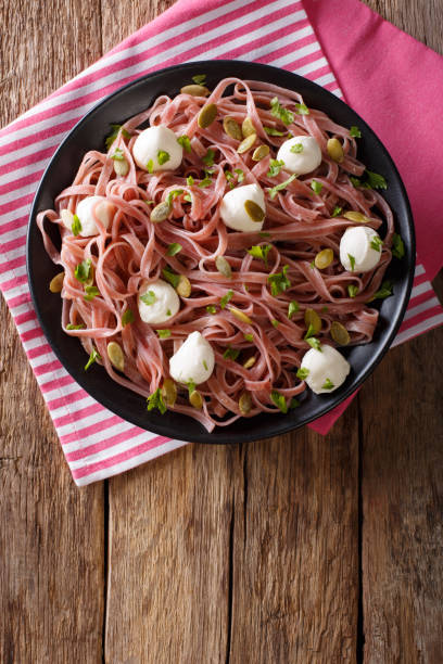 Beetroot pasta with mozzarella cheese, pumpkin seeds and greens close-up. Vertical top view