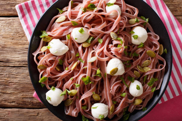 Noodles with beetroot juice with mozzarella, pumpkin seeds and greens close-up. horizontal top view