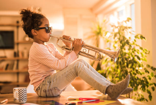 Cool African American girl having fun while playing trumpet at home.