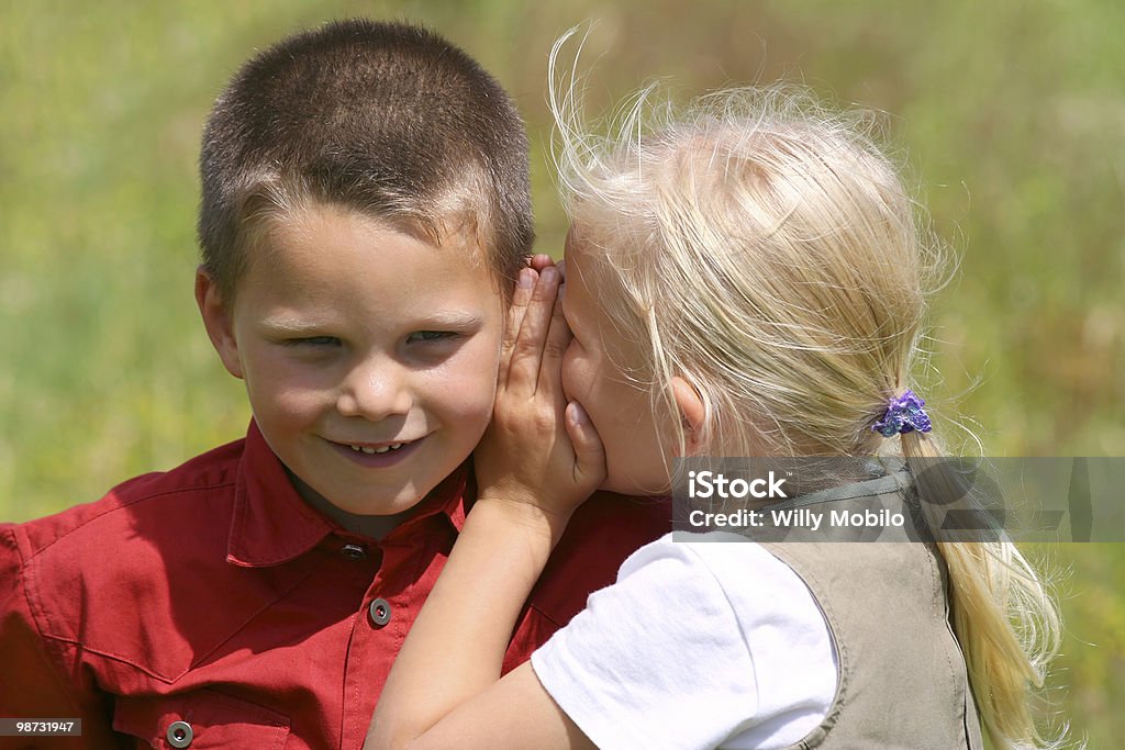 Whispering and smiling Girl whispering secret to a smiling boy. Blond Hair Stock Photo