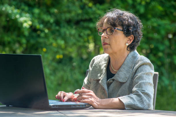 istock mature brunette using laptop in the garden 987323834