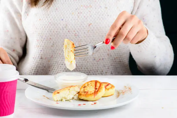 Unidentified woman eating appetizing sweet cottage cheese pancakes syrniki with jam and sour cream. Traditional Russian, Belarusian, Ukrainian breakfast