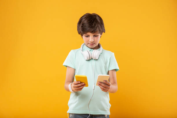 istock Concentrated schoolboy holding two phones 987359976