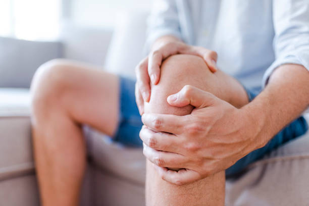 A mature man massaging his painful knee Man suffering from knee pain sitting sofa. A mature man massaging his painful knee. Man suffering from knee pain at home, closeup. Pain knee pain stock pictures, royalty-free photos & images