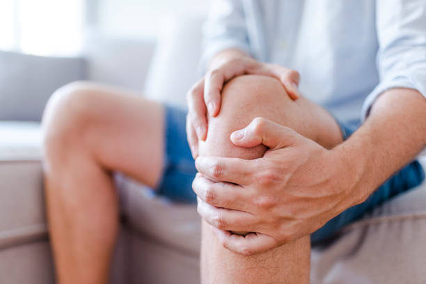 A mature man massaging his painful knee Man suffering from knee pain sitting sofa. A mature man massaging his painful knee. Man suffering from knee pain at home, closeup. Pain knee osteoarthritis stock pictures, royalty-free photos & images