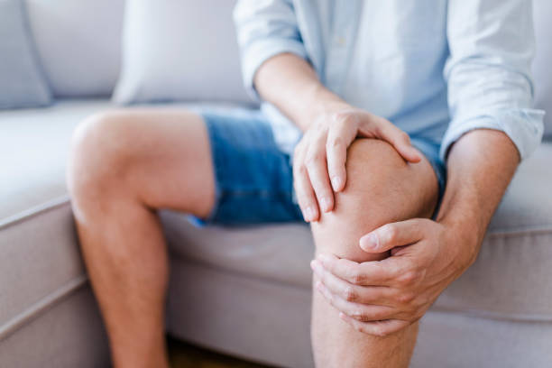 Man suffering from knee pain sitting sofa Man suffering from knee pain sitting sofa. A mature man massaging his painful knee. Man suffering from knee pain at home, closeup. Pain knee standing had to knee pose stock pictures, royalty-free photos & images