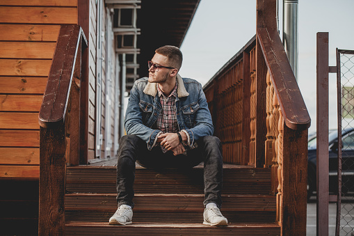 oung man sits on the porch of a wooden house