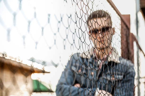 istock young man is standing behind a fence from a mesh 987399350