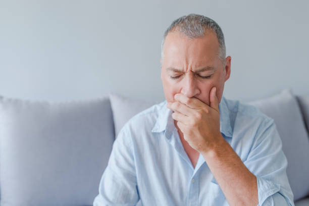 istock Frustrated young man touching his cheek and keeping eyes closed while sitting on the couch at home 987403962