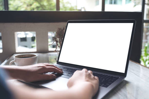 istock Mockup image of a woman using laptop with blank white desktop screen with coffee cup on table 987413162
