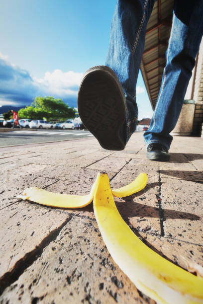 Foot about to step on discarded banana peel A banana skin lies on the sidewalk with a foot approaching it - an accident about to happen. slippery unrecognizable person safety outdoors stock pictures, royalty-free photos & images