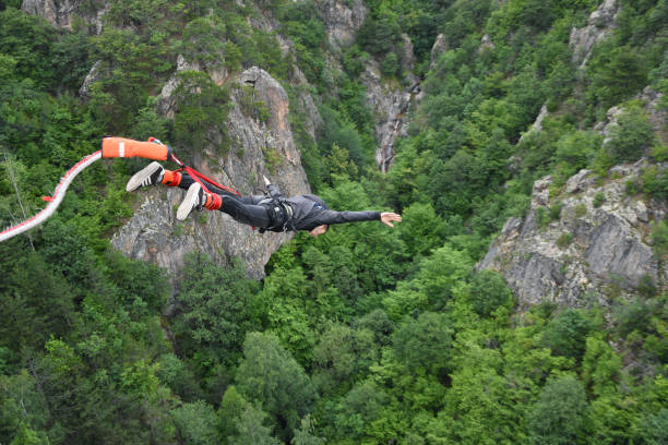 Bungee jump Klisura, Bulgaria - June 23, 2018: Young boy falling down performing bungee jump from 70 meters high bridge. Out of focus mountain cliff, rocks and green trees seen at background bungee jumping stock pictures, royalty-free photos & images