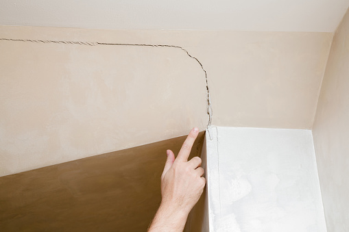 Man's hand finger pointing to the cracked wall in house. Building problems and solutions concept.
