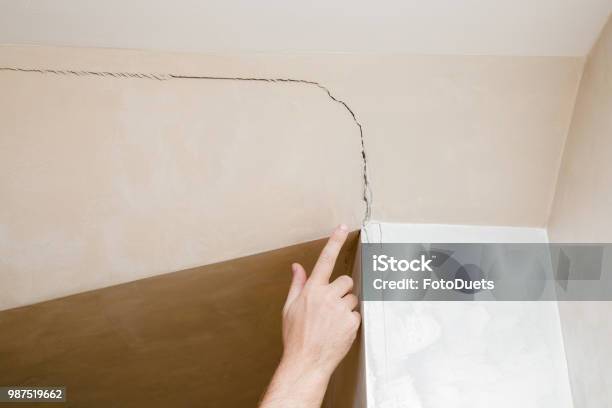 Mans Hand Finger Pointing To The Cracked Wall In House Building Problems And Solutions Concept Stock Photo - Download Image Now