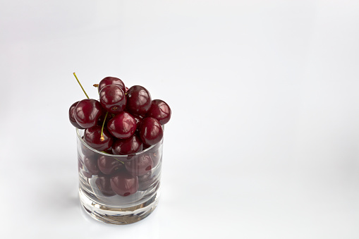 Ripe and red cherries are arranged in a clear glass on a light background, a picture in a high key