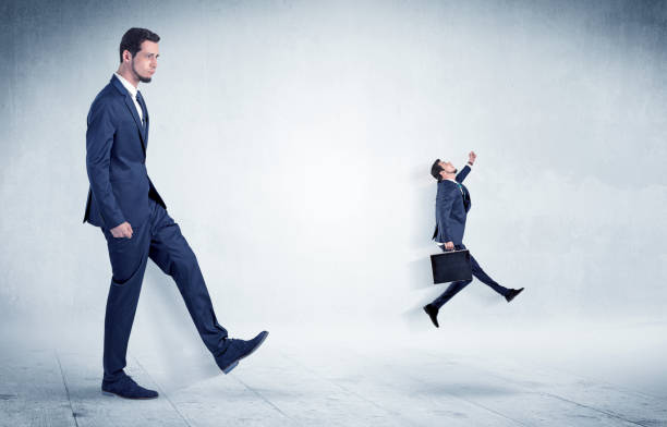 istock Big businessman kicking small businessman 987554098