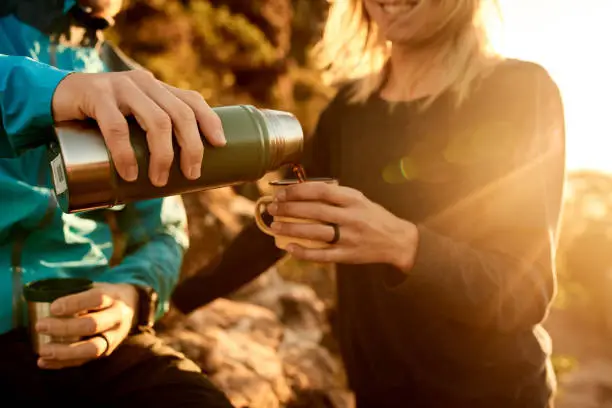 Cropped shot of an unrecognizable young couple taking a coffee break during their mountain hike