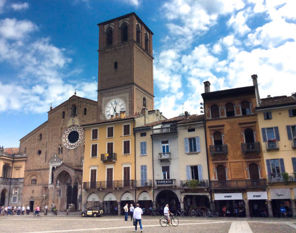 Lodi, Italy: Piazza Duomo with Pedestrians and Bicyclist Lodi, Italy: A bicyclist rides across Piazza Duomo at midday, while other people chat and walk on the piazza. The Duomo (mother church) and its bell tower are in the frame too. lodi italy stock pictures, royalty-free photos & images