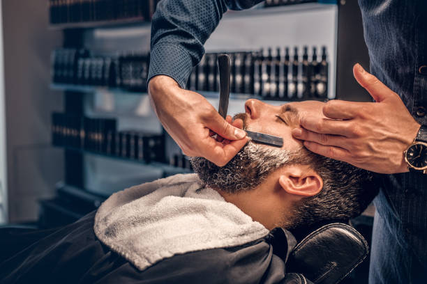 istock Barber shaving bearded male with a sharp razor. 987622072