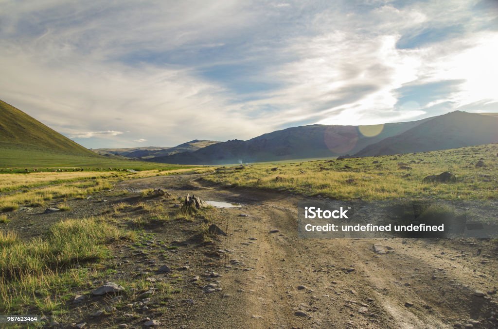 Mongolian Altai. Dirt road and mountain valley in beams of the evening sun. Smoking chimney of traditional yurt nomads. Nature and travel. Mongolia Bayan-Olgii Province Dirt Road Stock Photo