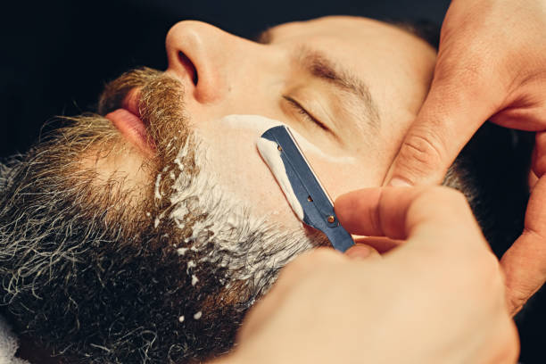 istock Barber shaving bearded male with a sharp razor. 987627598