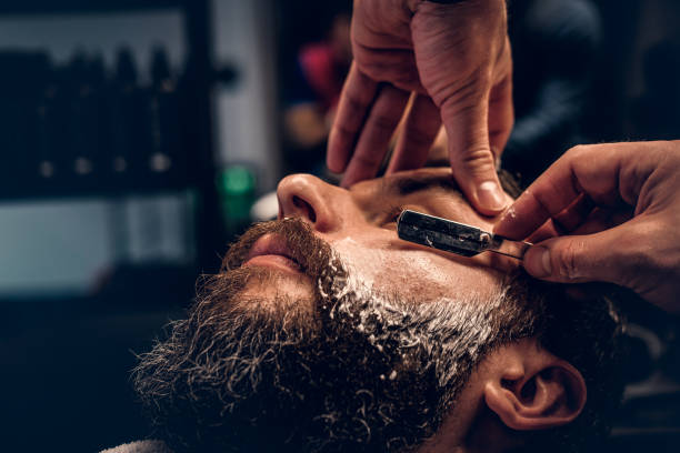 istock Barber shaving bearded male with a sharp razor. 987627876