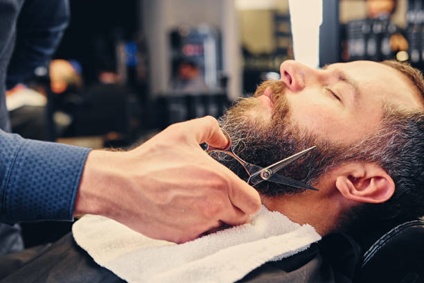 istock Stylish barber grooming a man's beard in a saloon. 987628132