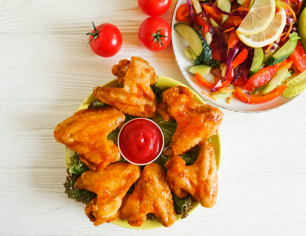 istock fried wings, salad on a wooden background 987654894