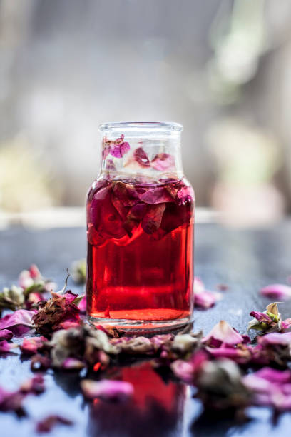 Rose water or Gulab jal or Gulab ka pani or Rosa water in a bottle on wooden surface with rose petals. stock photo