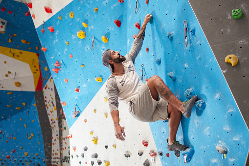 Low angle view of mature sporty man climbing wall in gym. Full length of fit male is exercising. He is in sports clothing.