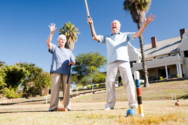 istock Senior man smiling after scoring while holding mallet in the air playing croquet 987709464