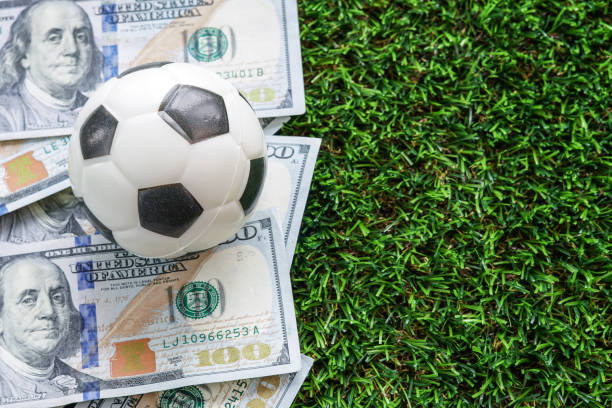Football Business Concept : A fooball on dollar bills and green grass background. Soccer gambling money concept. With copy space. stock photo