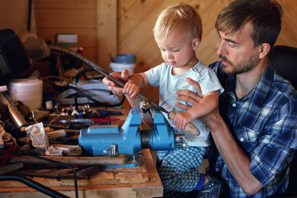 istock Father teaches his child to use tools vise and rasp in a workshop. Cute boy exploring new stuff. Fatherhood concept 987763644