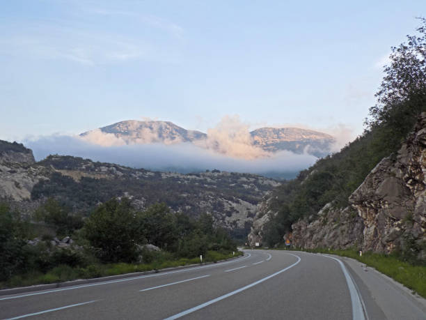 istock Double bend winding road in the mountains and Mountain peaks in the clouds 987781402