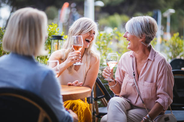 Happy senior women drinking wine and laughing together at restaurant Mature women enjoying a glass of wine, having fun and laughing together at city restaurant rosé wine stock pictures, royalty-free photos & images