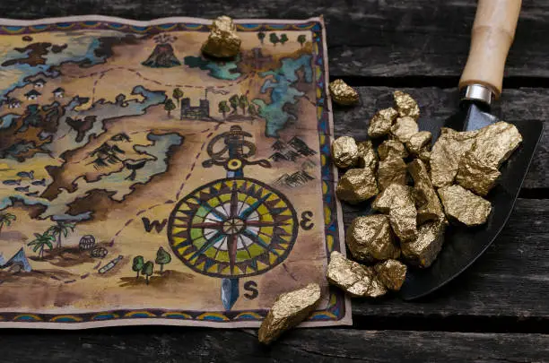 Treasure map and shovel full of gold nuggets ore on wooden table. Treasure hunter or gold miner concept.