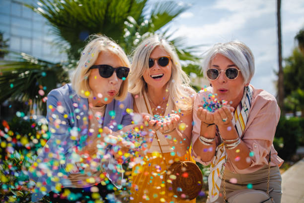 femmes âgées joyeuses célébrant en soufflant les confettis dans la ville - friendship senior adult caucasian cheerful photos et images de collection