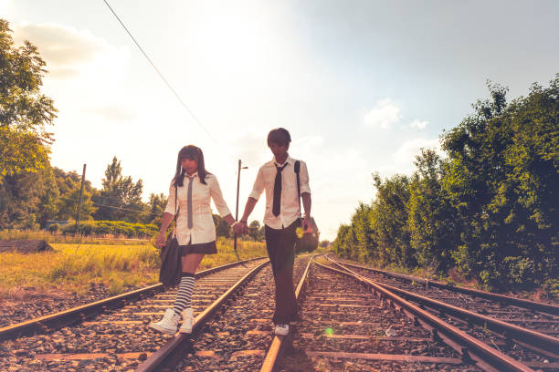 istock asian couple with school uniforms walking on a railroad 987822546
