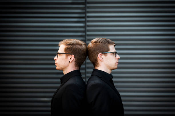 twin brothers portrait back on back twin brothers with black suits and glasses standing back on back in urban surrounding. two men same clothes stock pictures, royalty-free photos & images