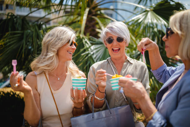donne mature che mangiano gelato mentre fanno shopping in città - bag senior adult outdoors friendship foto e immagini stock