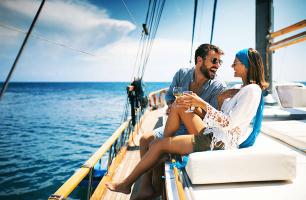 Couple on a sailboat. Closeup side view of a young couple relaxing on a sailboat cruise while sailing close to the coast. They are having some wine and laughing. honeymoon stock pictures, royalty-free photos & images