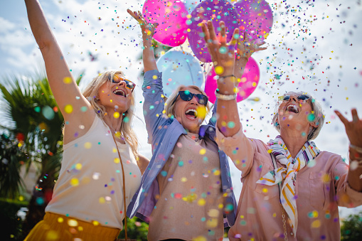 Happy fashionable senior friends having fun celebrating with balloons and throwing confetti in the city