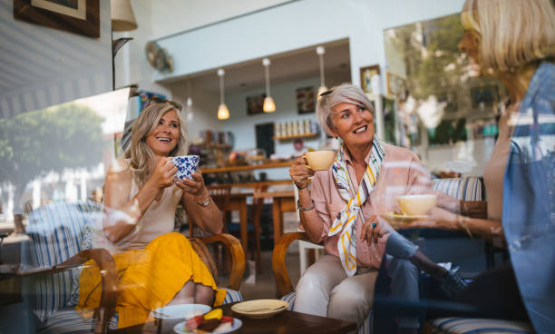 istock Smiling mature women having fun drinking coffee together at cafe 987886980
