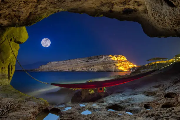 Cave with hammock at night with full moon, Matala, Crete, Greece.