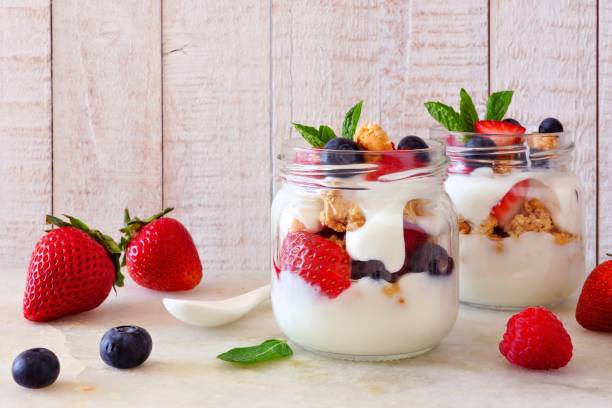 istock Berry parfaits in mason jars. Side view scene on white wood. 987929592