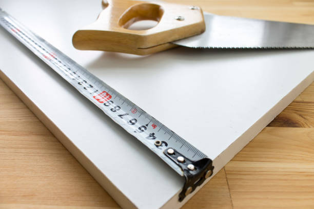 istock Wooden background with a handsaw and tape ruler lying on white panel 987929616