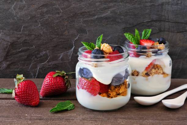 Berry parfaits in mason jars. Side view scene on dark background.