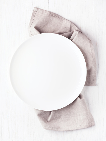Empty white circle plate on wooden table with linen napkin. Overhead view, mock up.