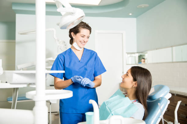 sourire dentiste en uniforme parlant à la fille à la clinique - dentist teenager dental hygiene sitting photos et images de collection